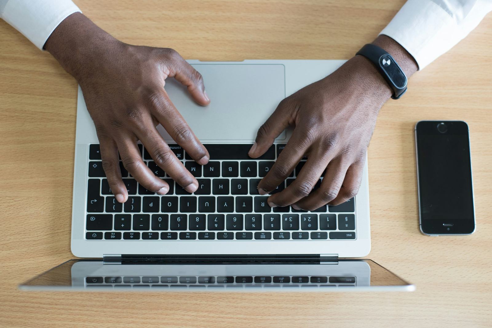 Hands typing on a laptop beside a phone