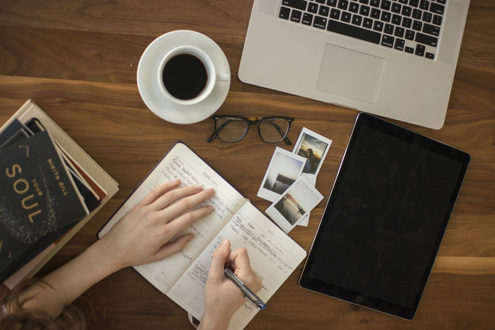 Hands writing a plan in a notebook beside a laptop